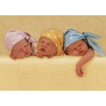 Anne Geddes 1000 gabaliņu puzle ar trim mazuļiem krāsainās cepurītēs uz dzeltena fona.
