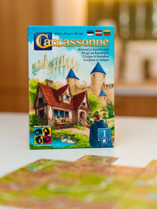 Carcassonne paplašinājuma Krogi un katedrāles spēles kaste ar ilustrētu viduslaiku pilsētas un kroga dizainu.