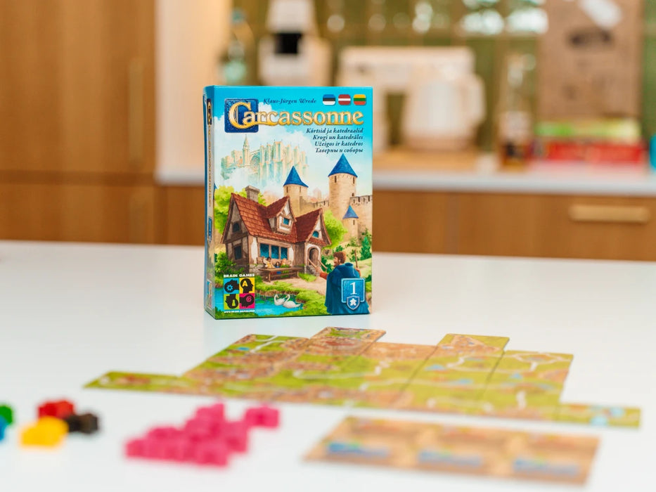 Carcassonne paplašinājuma Krogi un katedrāles kaste ar spēles lauciņiem un krāsainām koka figūriņām uz galda.