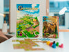 Carcassonne pamatspēle un paplašinājums Tirgoņi un būvnieki ar krāsainiem spēles lauciņiem un koka figūriņām uz galda.