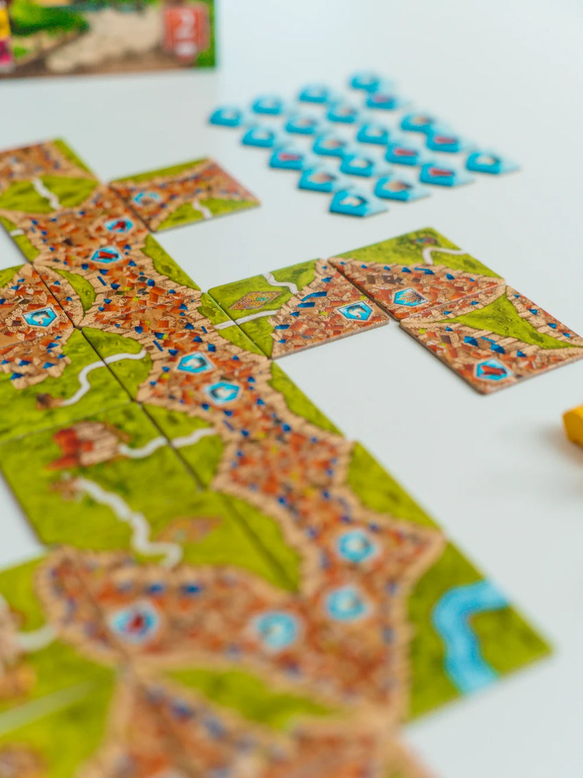 Carcassonne paplašinājuma Tirgoņi un būvnieki kartona lauciņi ar pilsētu, ceļu un preču simboliem uz balta fona.