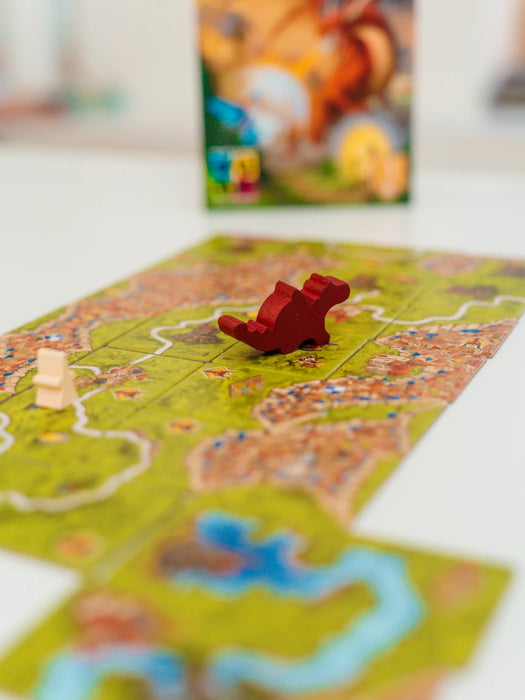 Carcassonne paplašinājuma spēles laukums ar sarkanu koka pūķa figūriņu un spēles kasti fonā.