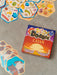 Dobble CATAN galda spēles kaste ar sešstūrainām kārtīm, kurās attēloti dažādi spēles simboli uz pelēka fona.