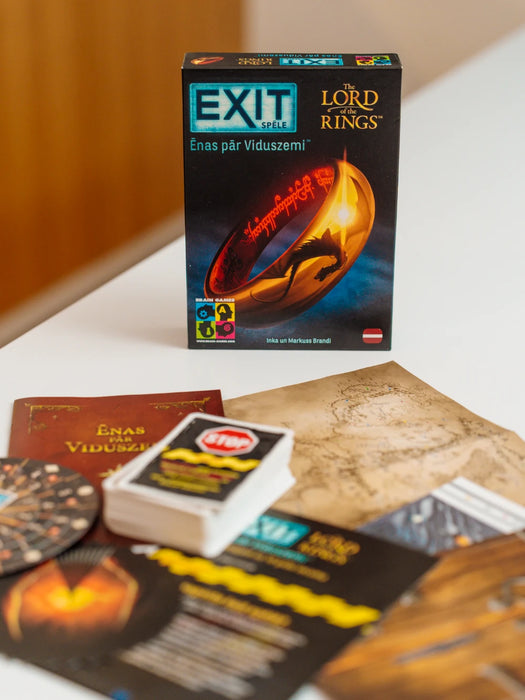 EXIT Gredzenu pavēlnieks galda spēles kaste ar kartēm, mīklu materiāliem un Viduszemes karti uz balta galda.