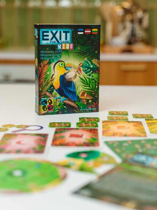 EXIT Kids: Mīklainie džungļi galda spēles kaste ar tukānu un izkārtotas krāsainas mīklu kārtis uz balta galda.