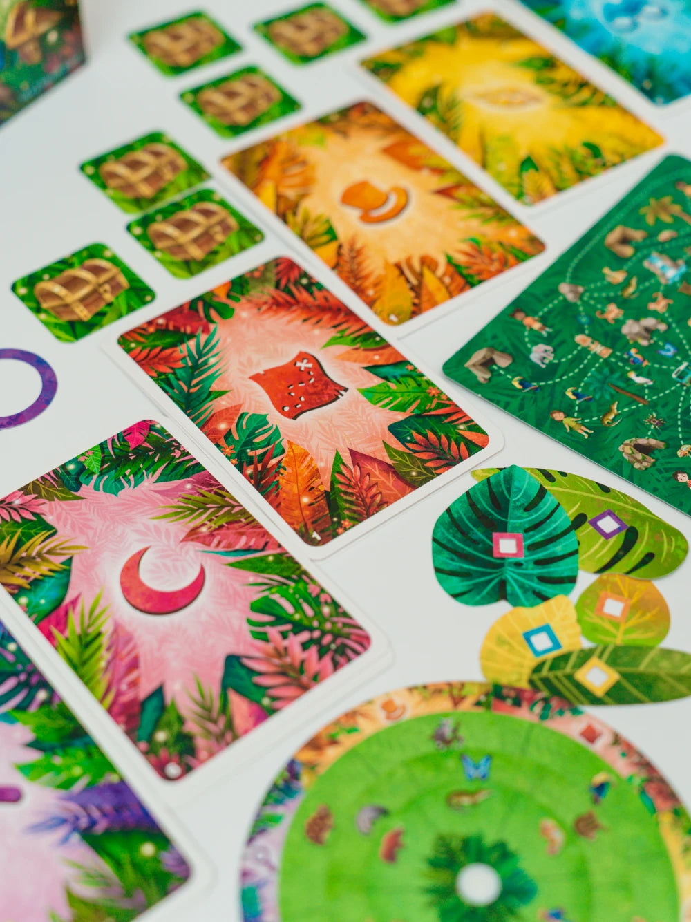 EXIT Kids: Mīklainie džungļi galda spēles kārtis ar krāsainām džungļu ilustrācijām, dārgumu lādēm un mīklu elementiem.