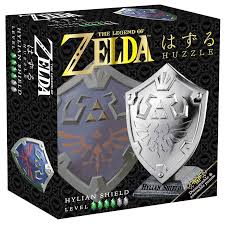 Sudrabota metāla Huzzle Hylian Shield prāta spēle Zelda iepakojumā ar detalizētu vairoga dizainu un sarežģītības līmeni.