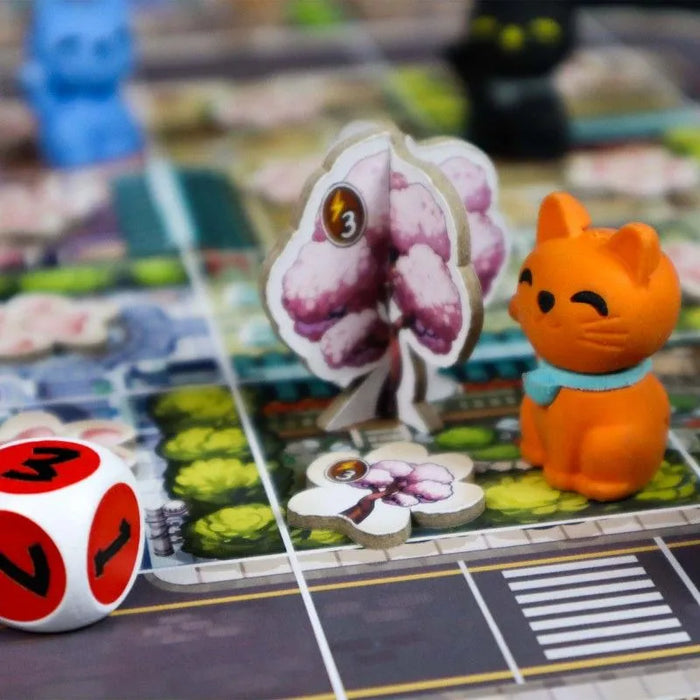 Kyoto no Neko galda spēle ar oranžu kaķēna figūriņu, kartona koka elementiem un spēļu kauliņu uz krāsaina pilsētas kartes laukuma.