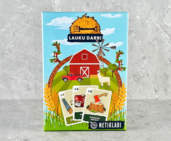 Lauku Darbi kāršu spēles kaste ar košu lauku sētas ilustrāciju, sarkano šķūni un spēļu kārtīm uz pelēka fona.