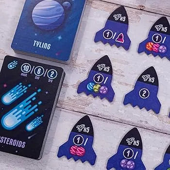 Point Galaxy galda spēles kārtis un zilas raķešu formas žetoni ar planētu simboliem uz koka galda virsmas.