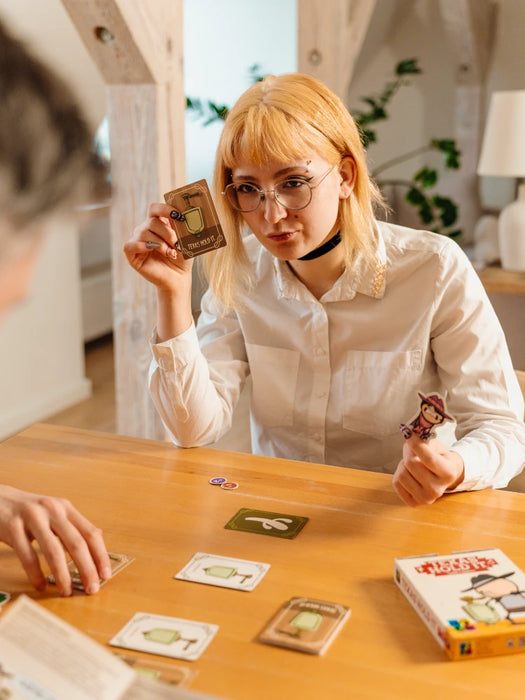 Jauna sieviete spēlē kāršu spēli Texas Hold It, turot rokās spēles kārtis ar pisuāra un kovboja ilustrācijām pie koka galda.