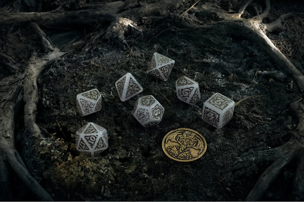 Balti Witcher Leshen kauliņu komplekts ar tumšiem rotājumiem un metāla monētu uz meža zemes fona.