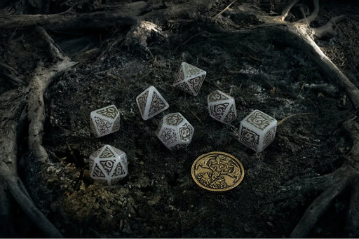 Balti Witcher Leshen kauliņu komplekts ar tumšiem rotājumiem un metāla monētu uz meža zemes fona.