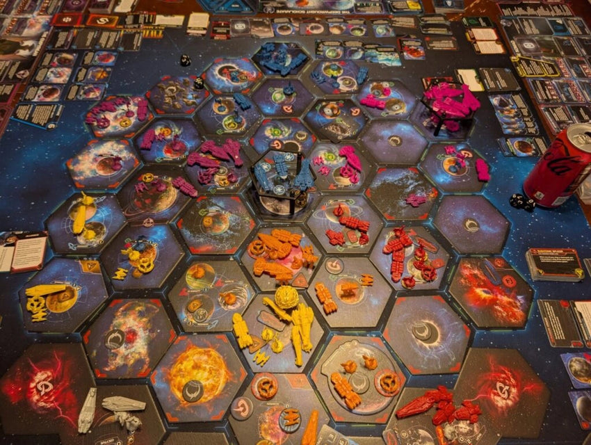 Twilight Imperium galda spēle ar krāsainām plastmasas kosmosa kuģu figūriņām uz sešstūrainiem galaktikas sektoru laukumiem.